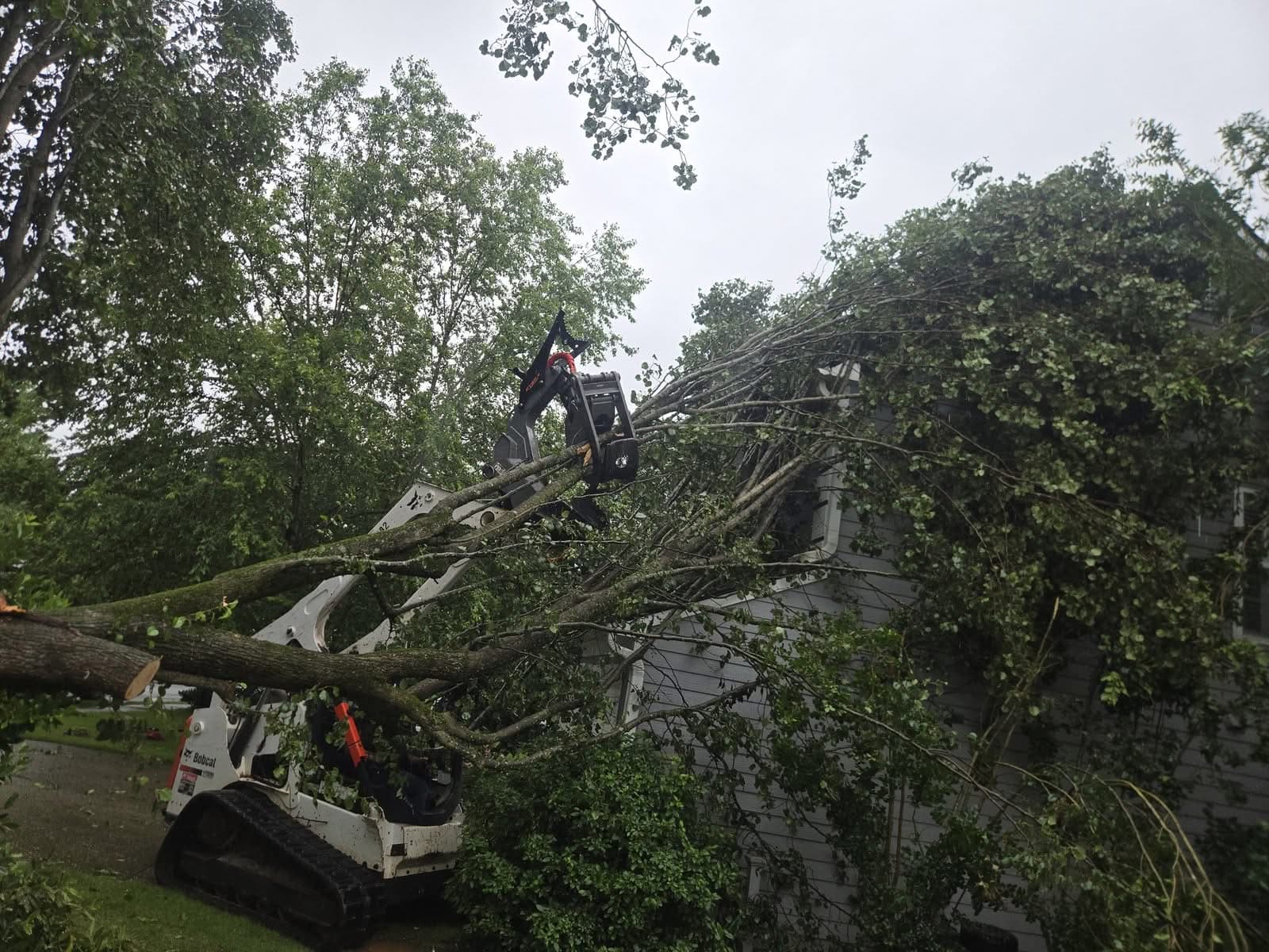 Skid steer grapple lifting broken limbs off a house wall in Acworth GA, June 2026