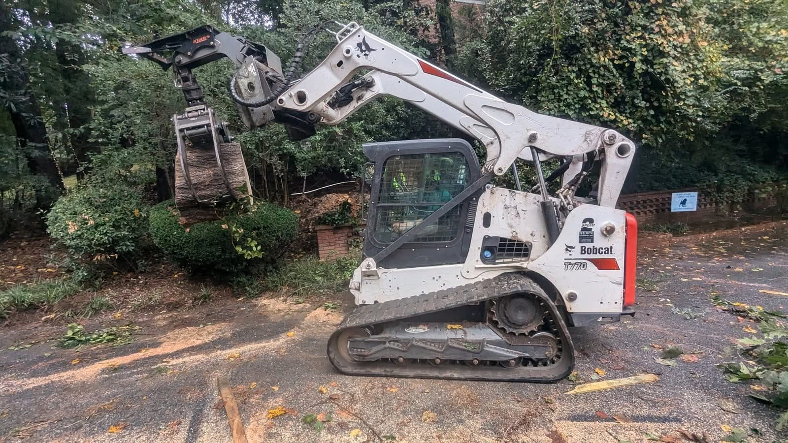 Bobcat T770 skid steer with grapple carrying a log section down a driveway in Atlanta GA, September 2024
