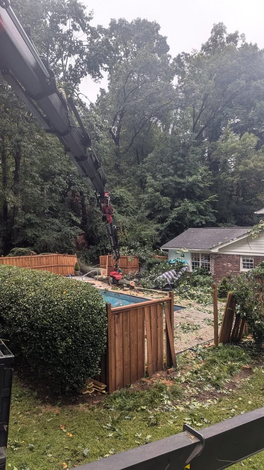 Crane with grapple saw lifting sectioned trunk pieces off a pool deck in Atlanta GA, September 2024