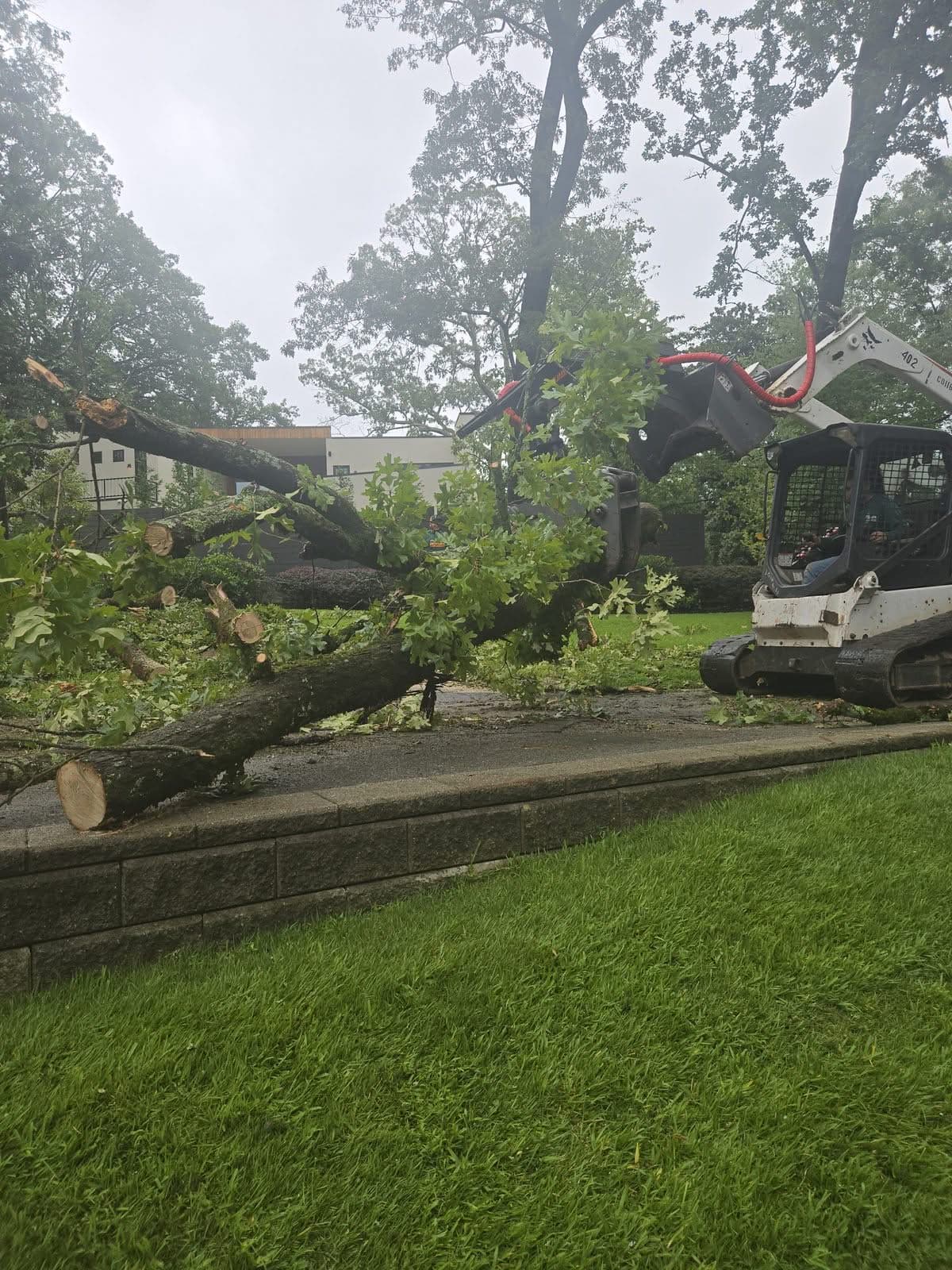 Grapple loader lifting a broken oak limb away from a house
