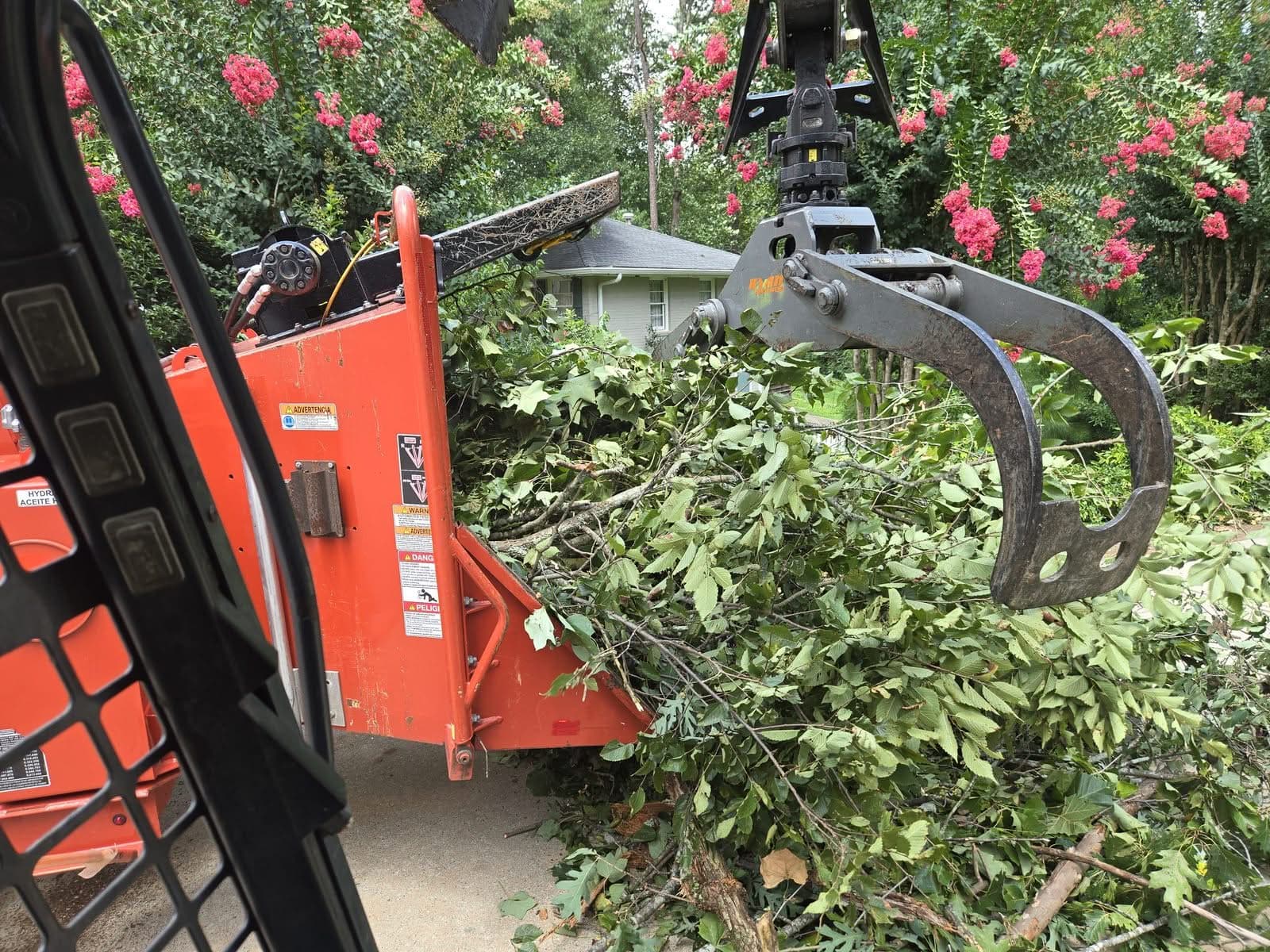 Hydraulic grapple feeding brush into an orange wood chipper