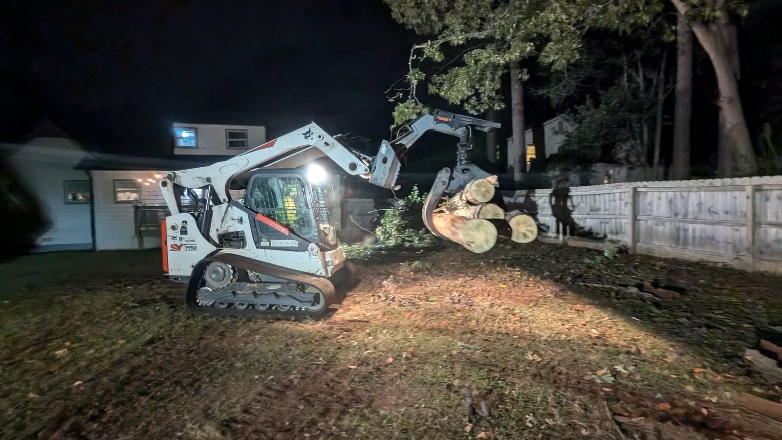 Skid steer with grapple carrying log sections at night in Kennesaw GA, September 2024