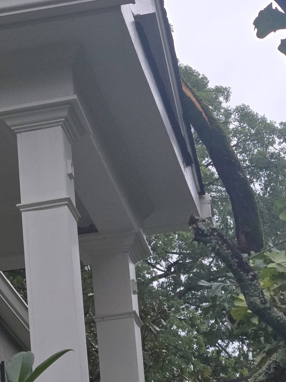 Broken tree limb lodged against a porch soffit and roof edge