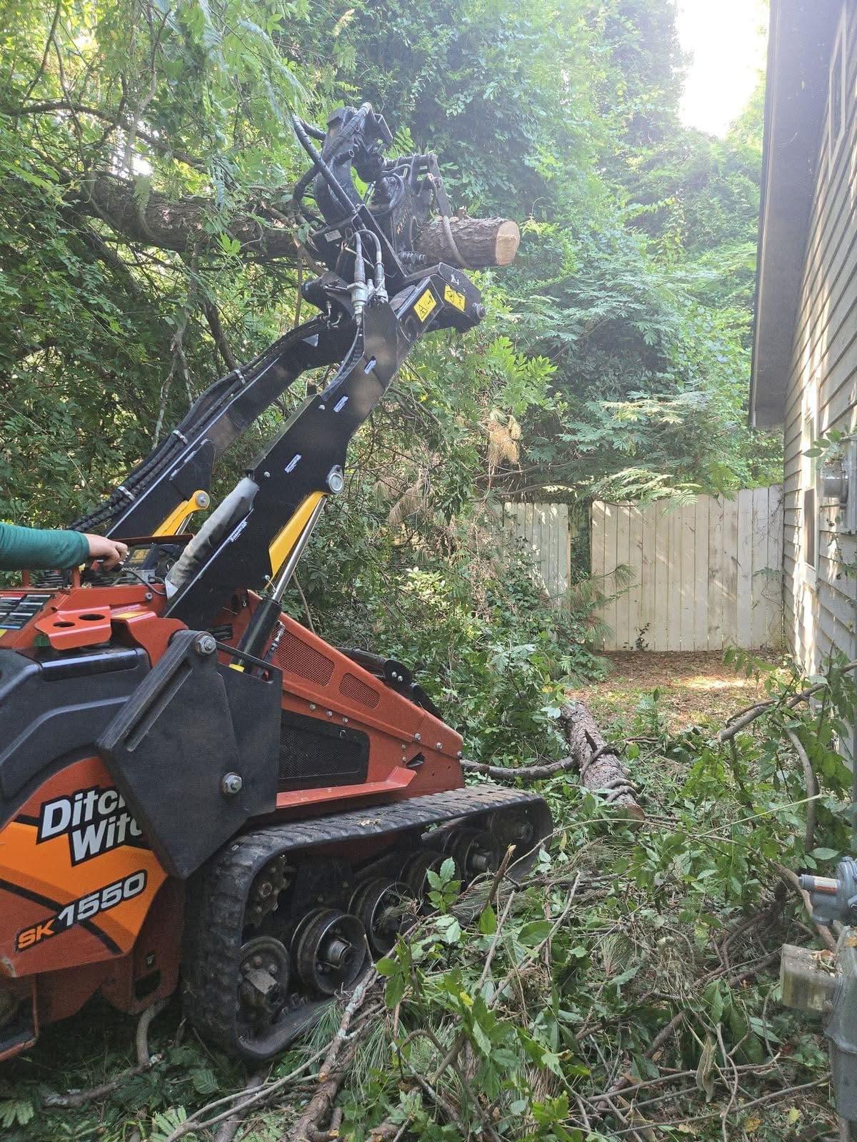 Mini skid steer carrying log sections through a Marietta GA side yard, July 2025