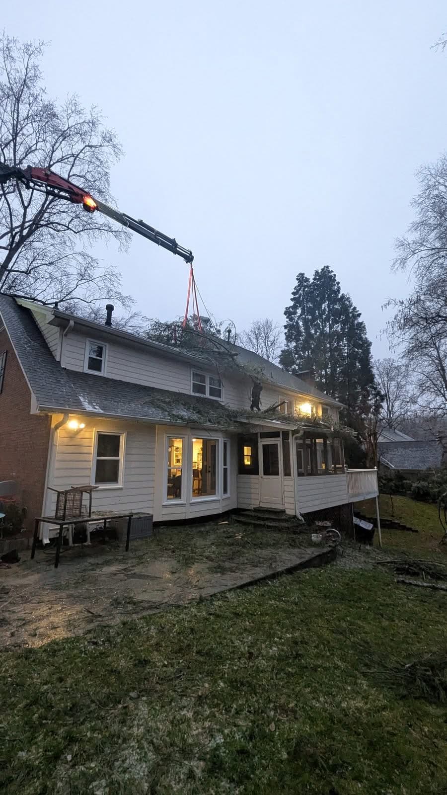 Crane lifting tree sections off a roof at dusk with climber working in Roswell GA, January 2026