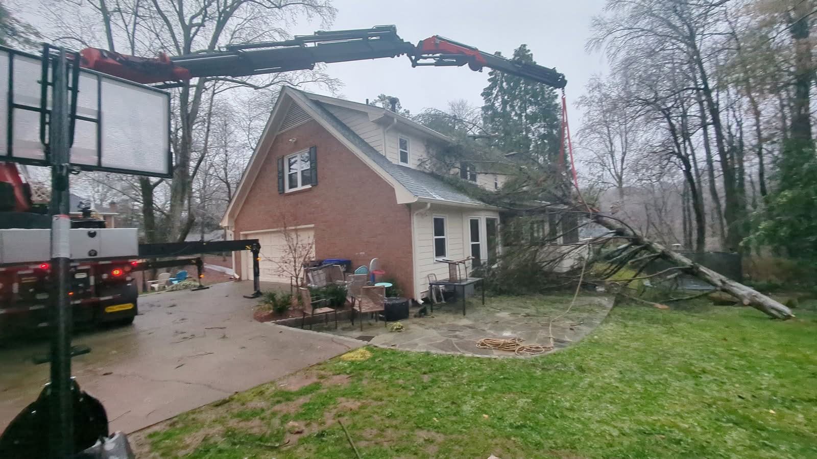Knuckleboom crane boom extended over the roof and rigged with slings to a fallen pine in Roswell GA, January 2026
