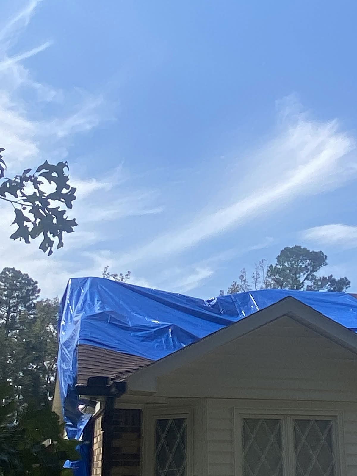 Blue tarp secured over a damaged roof section after tree removal