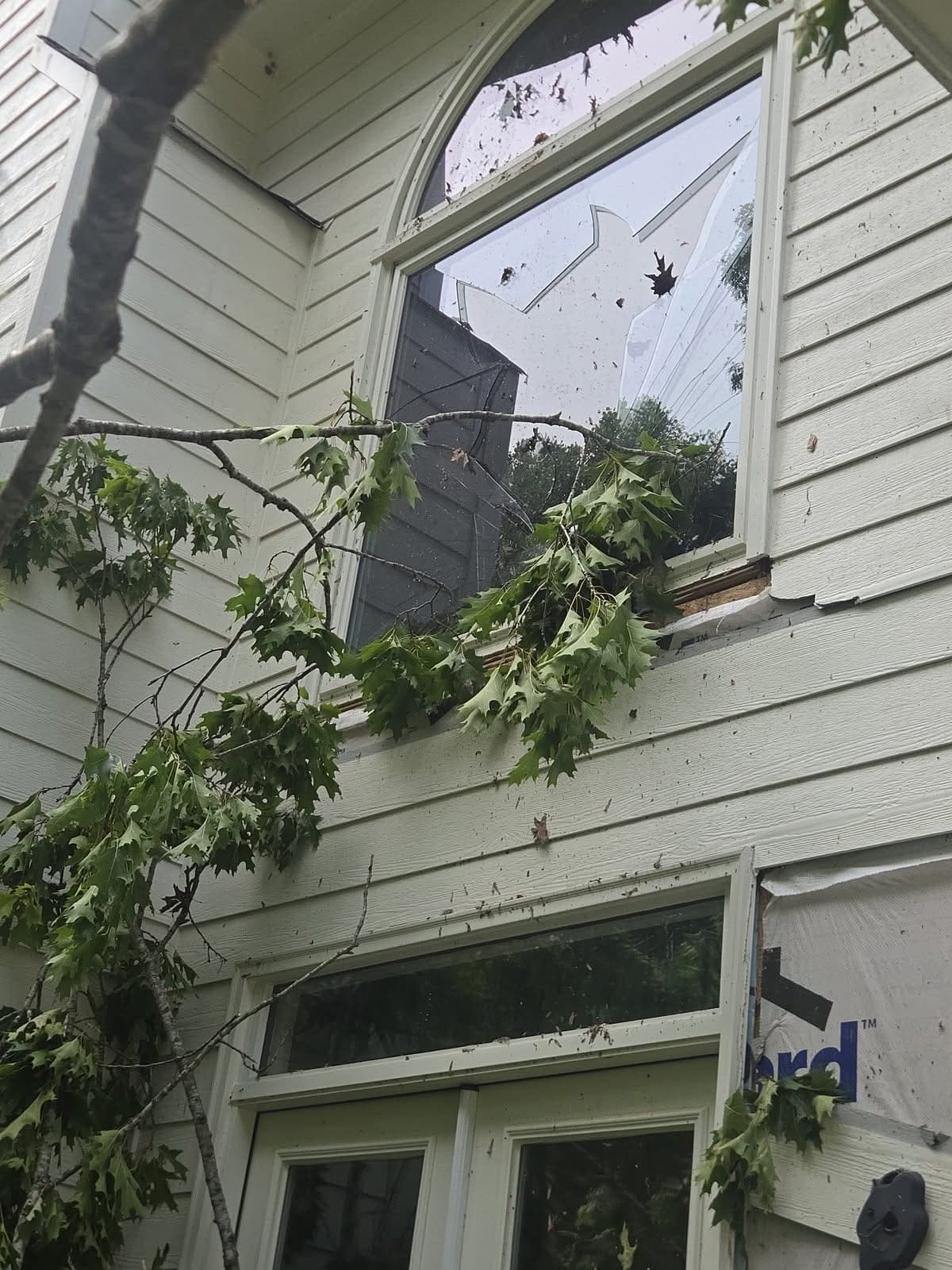 Shattered upper window with oak branches after a tree fell on a house in Woodstock GA, May 2026