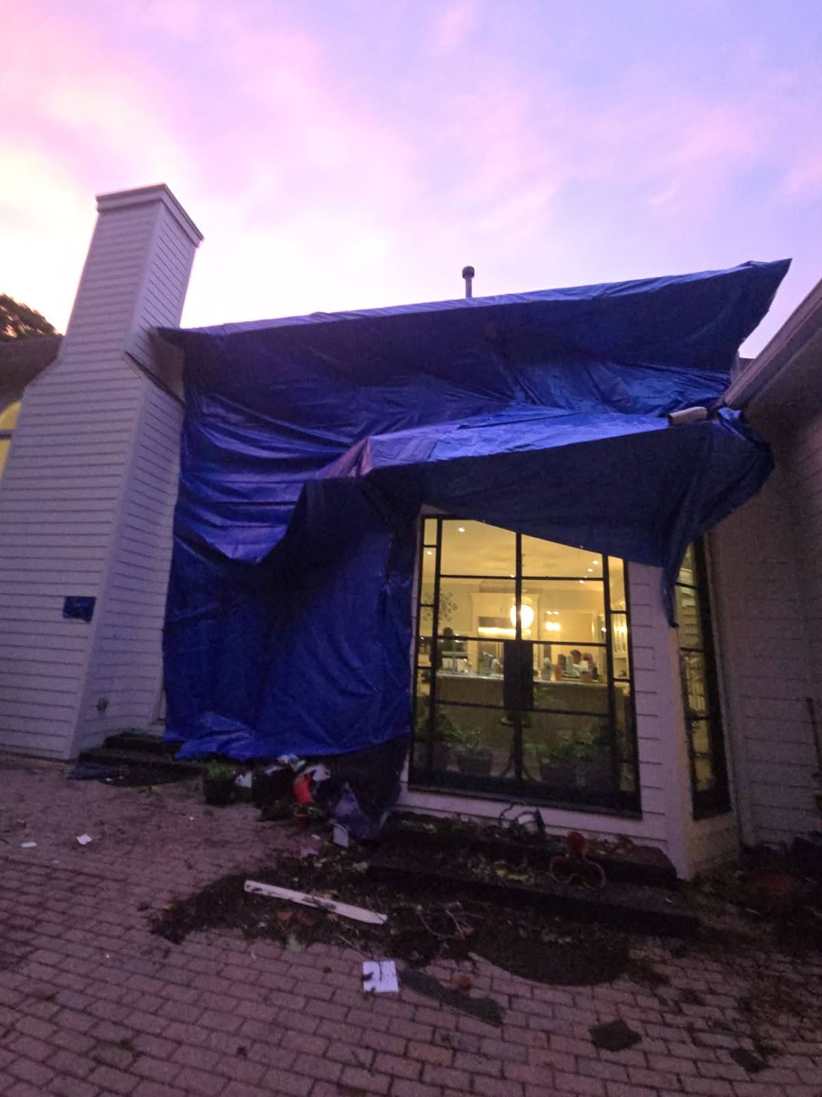 House roof and wall covered with tarps at dusk after emergency tree removal in Woodstock GA, May 2026
