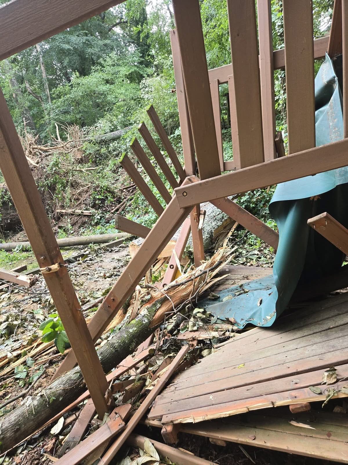 Broken rails and decking of a wooden backyard play structure crushed by a fallen tree