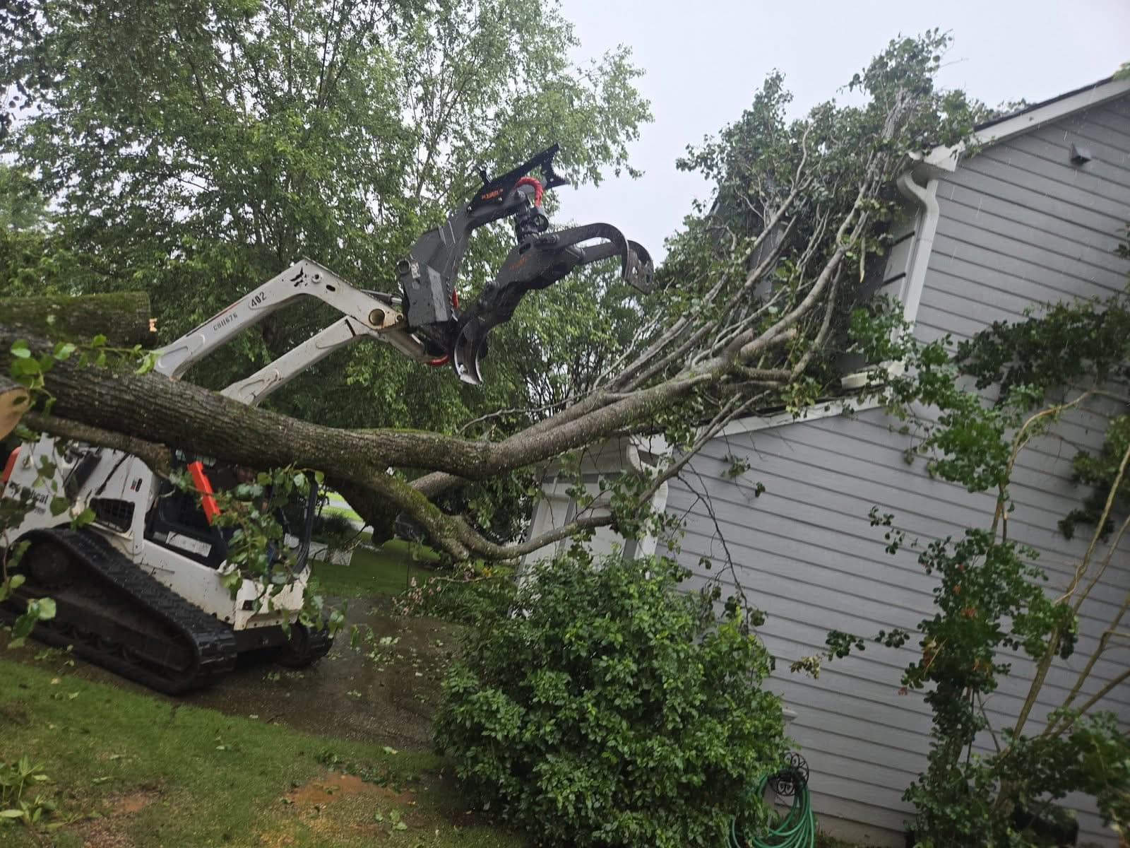 Skid steer grapple reaching over a storm-fallen tree resting on a house in Acworth GA, June 2026