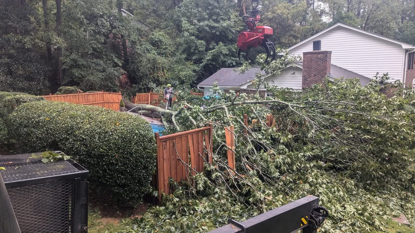 Storm-fallen oak lying across a privacy fence and pool deck with grapple saw descending in Atlanta GA, September 2024