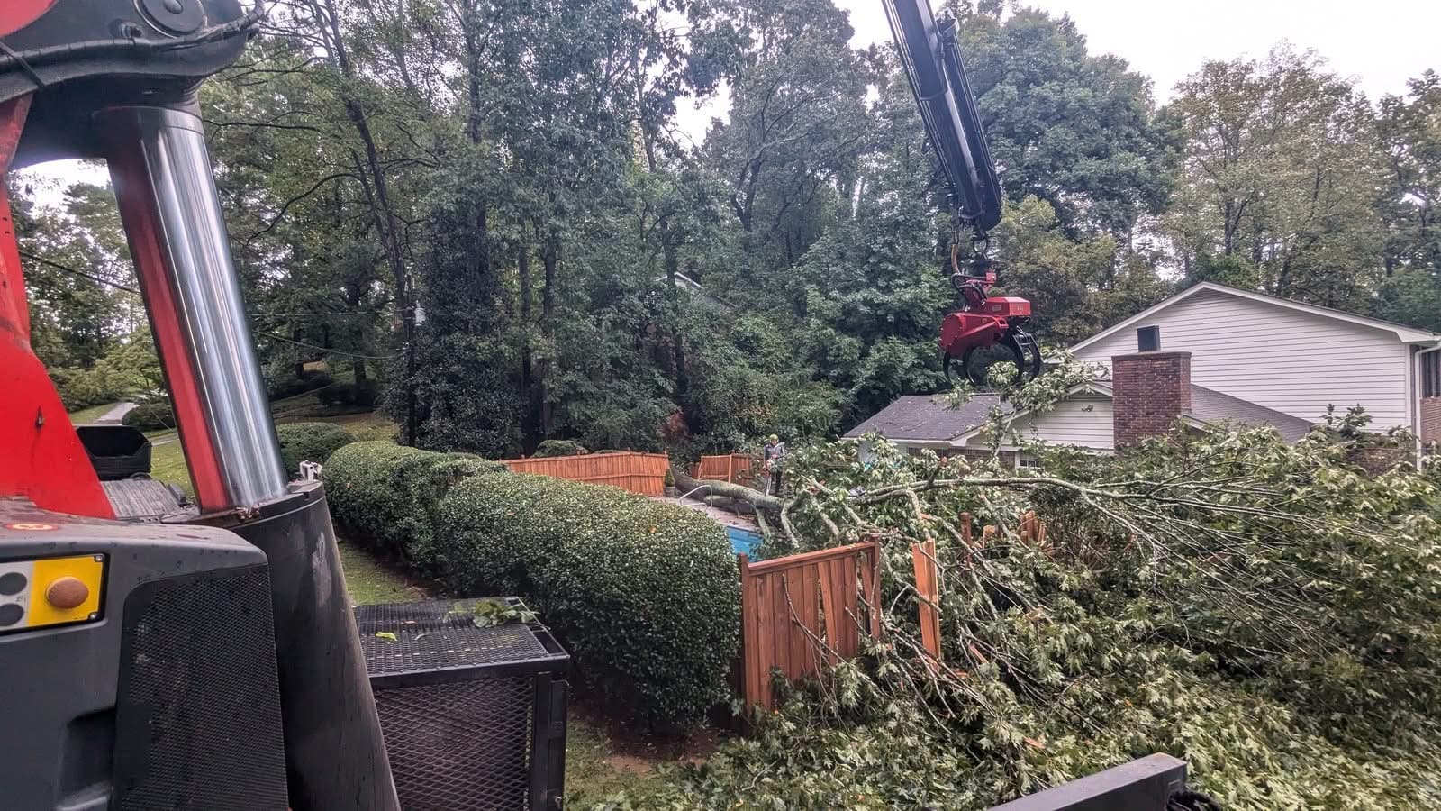 Grapple-saw crane head positioned over a storm-fallen oak on the backyard fence and pool in Atlanta GA, September 2024