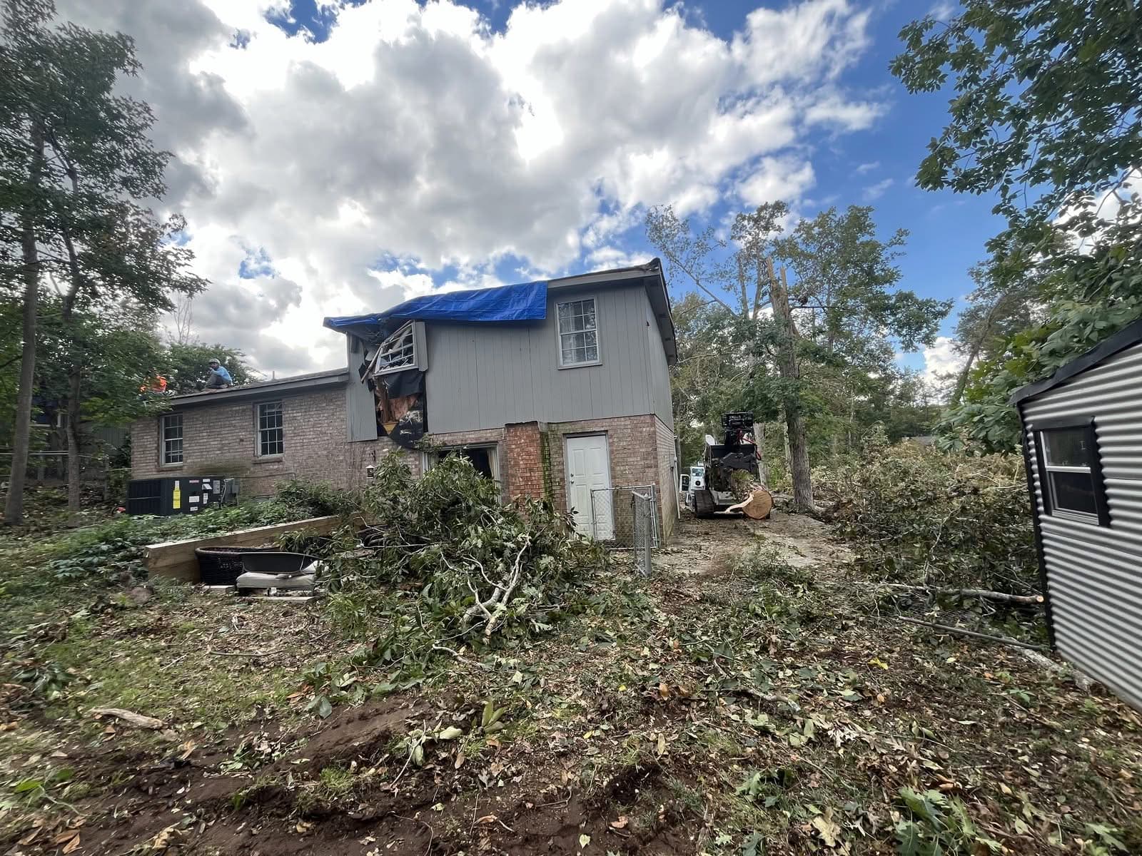 Storm-damaged house with tarped roof and upper window during tree removal