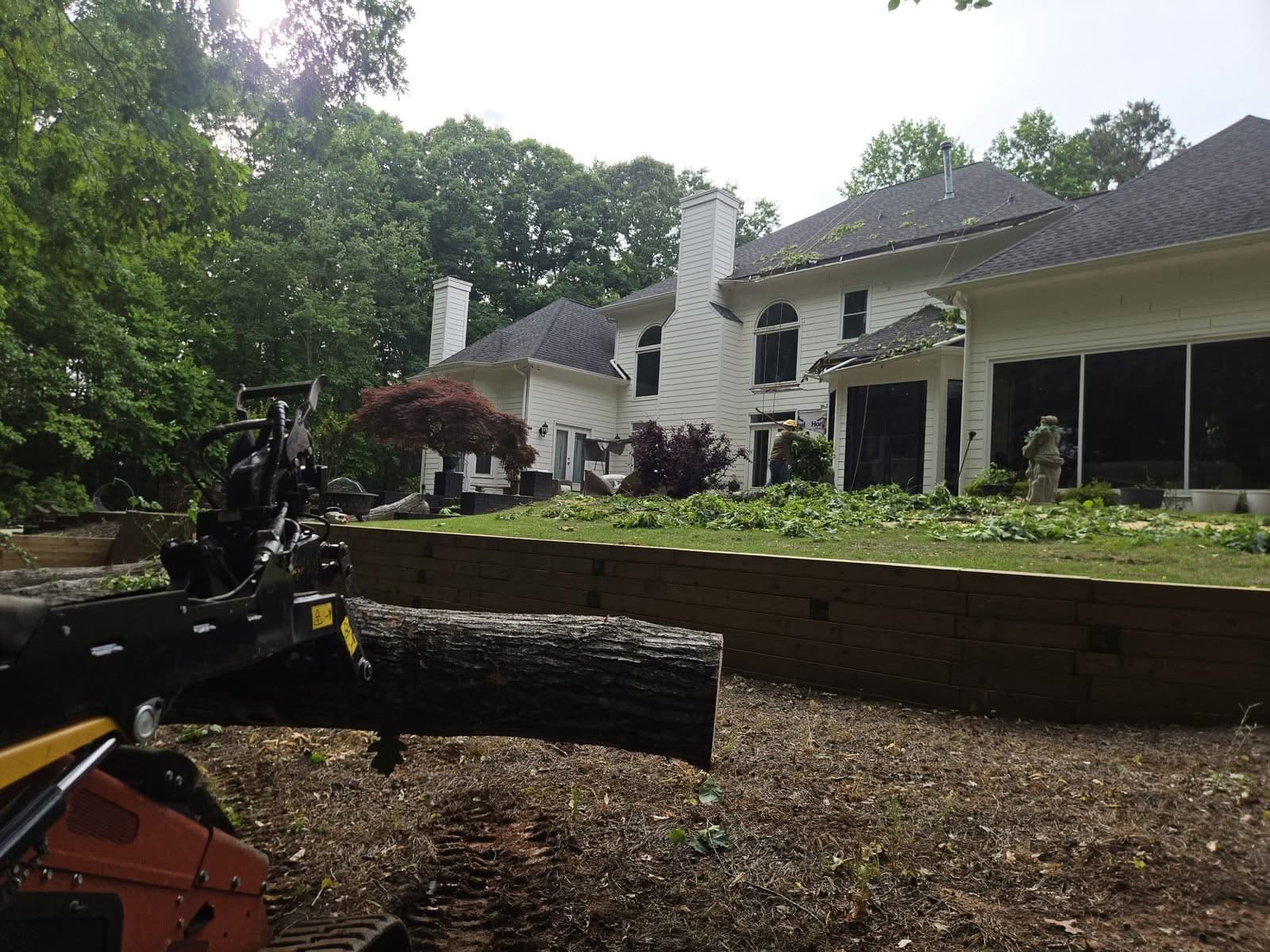Tree removal crew and mini skid steer carrying an oak trunk section away from a house in Woodstock GA, May 2026