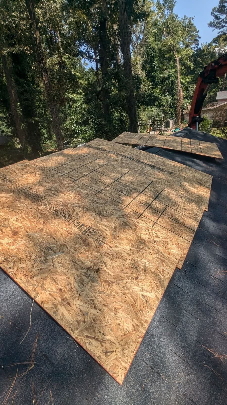 Roof decked over with fresh sheathing after emergency tree removal, crane arm overhead